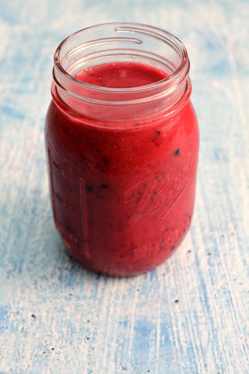Bright pink smoothie in a jar on a blue background, close up.