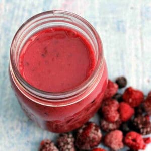 Red smoothie in a glass jar, berries beside it.