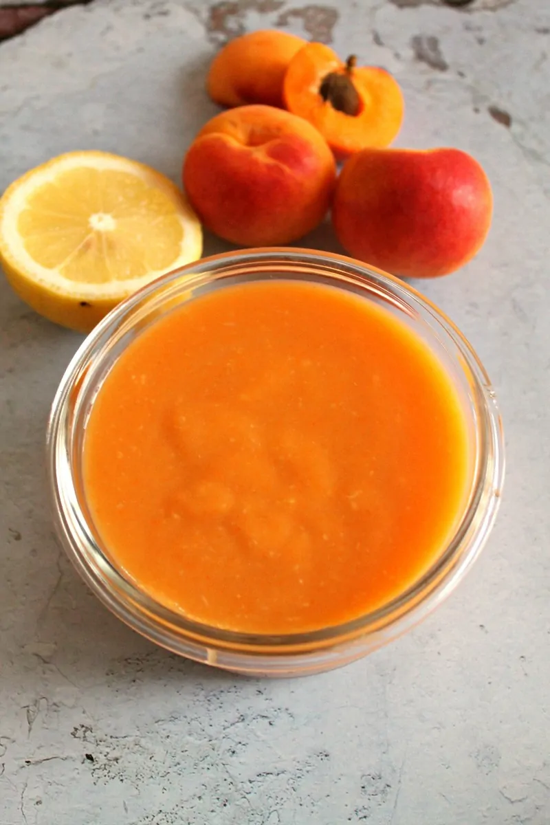 Pot of apricot curd with apricots and lemon behind it.