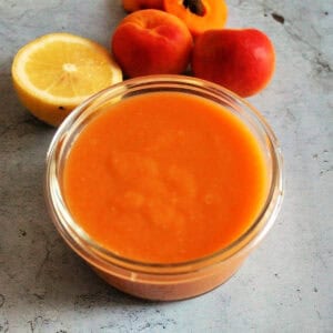 Apricot curd in a glass bowl, fresh apricots and half a lemon behind.