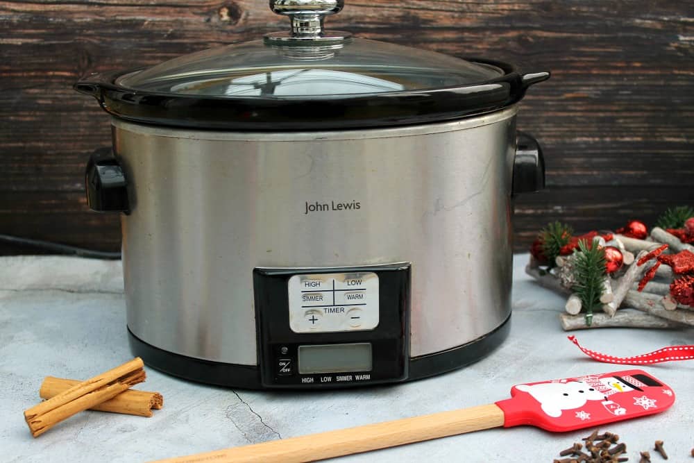 Slow cooker surrounded by Christmas decorations and utensils.