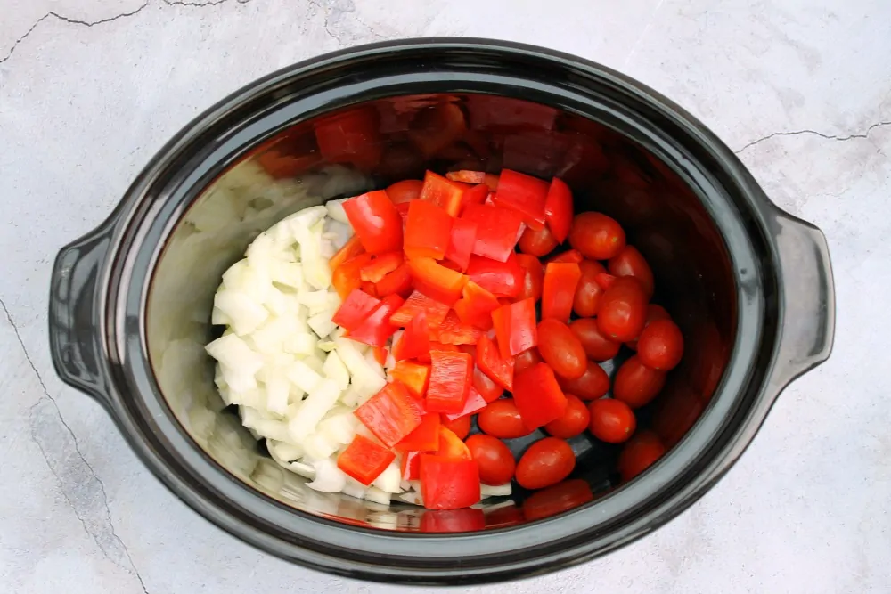 Slow cooker pot with chopped onion, red pepper and baby tomatoes.