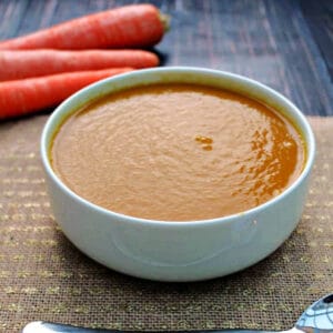 Bowl of carrot soup with carrots behind it.