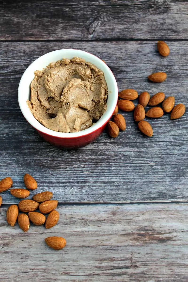 Almond butter in a small pot, with almonds around it.
