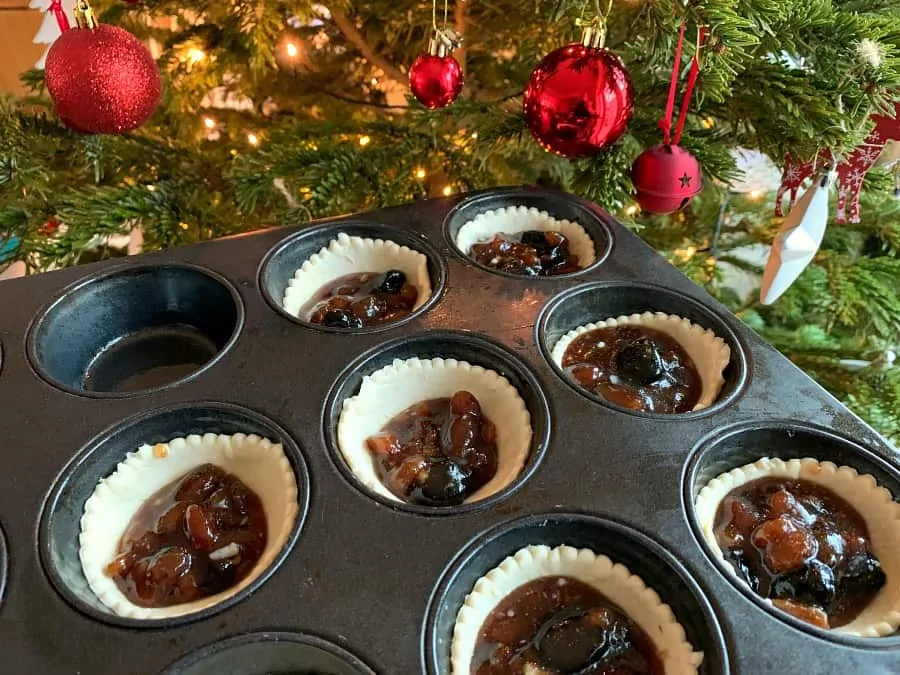 Mince pie bases filled with mincemeat with Christmas tree in background.