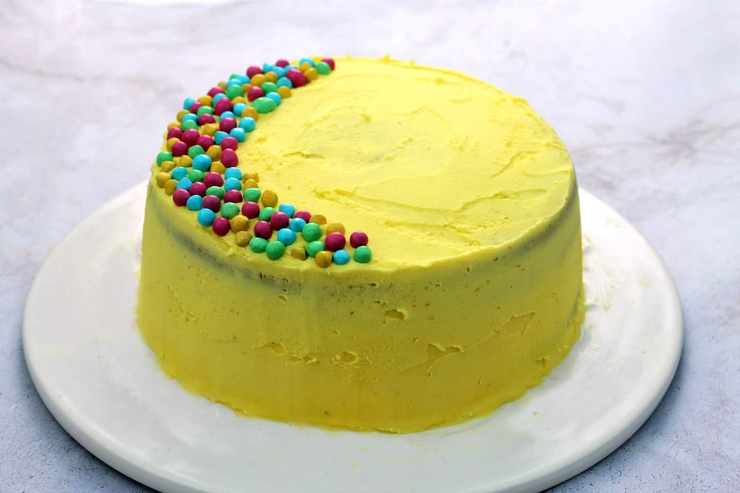Side view of cake with yellow frosting and multicoloured sprinkles.