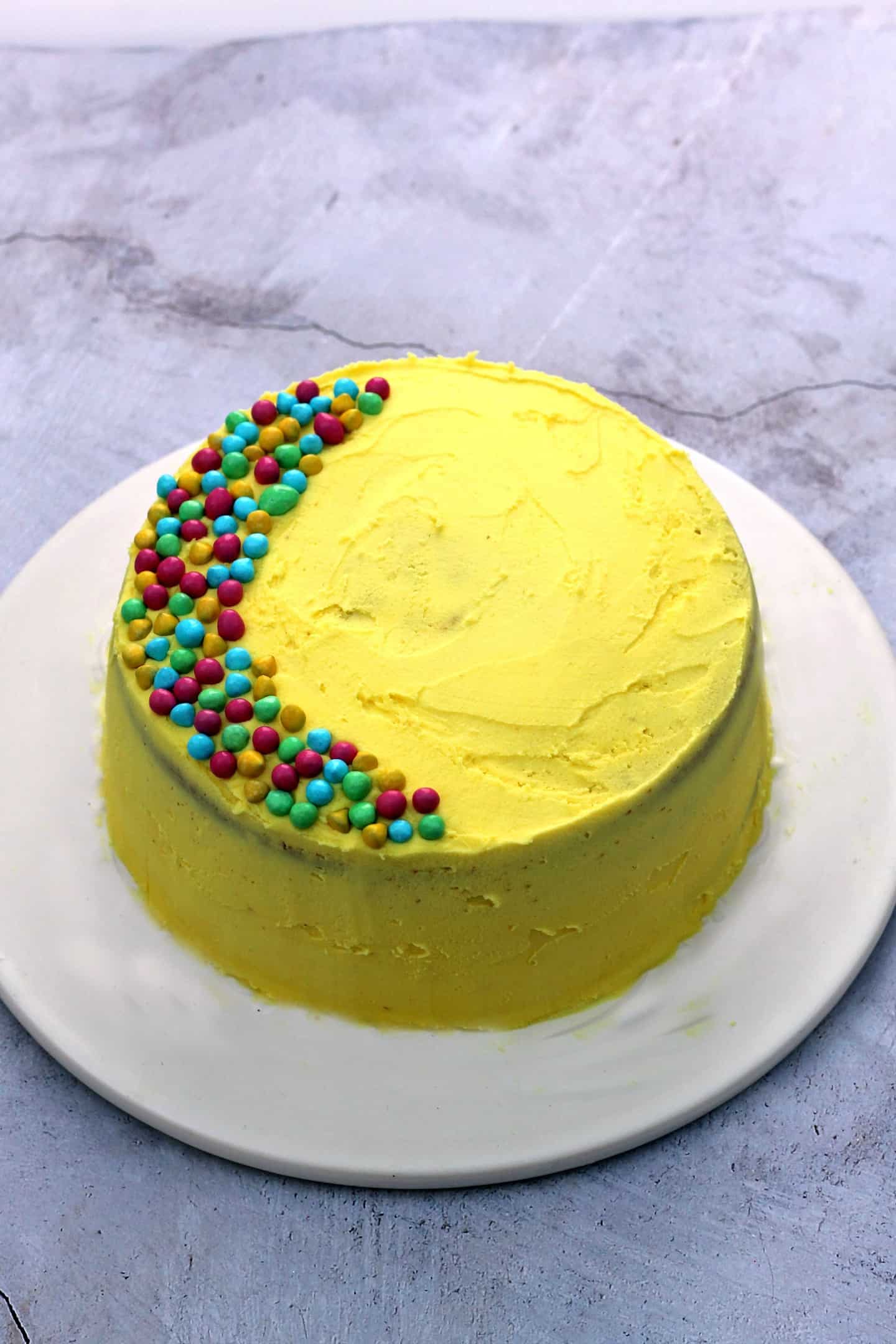 View of a yellow birthday cake with sprinkles on a white plate.