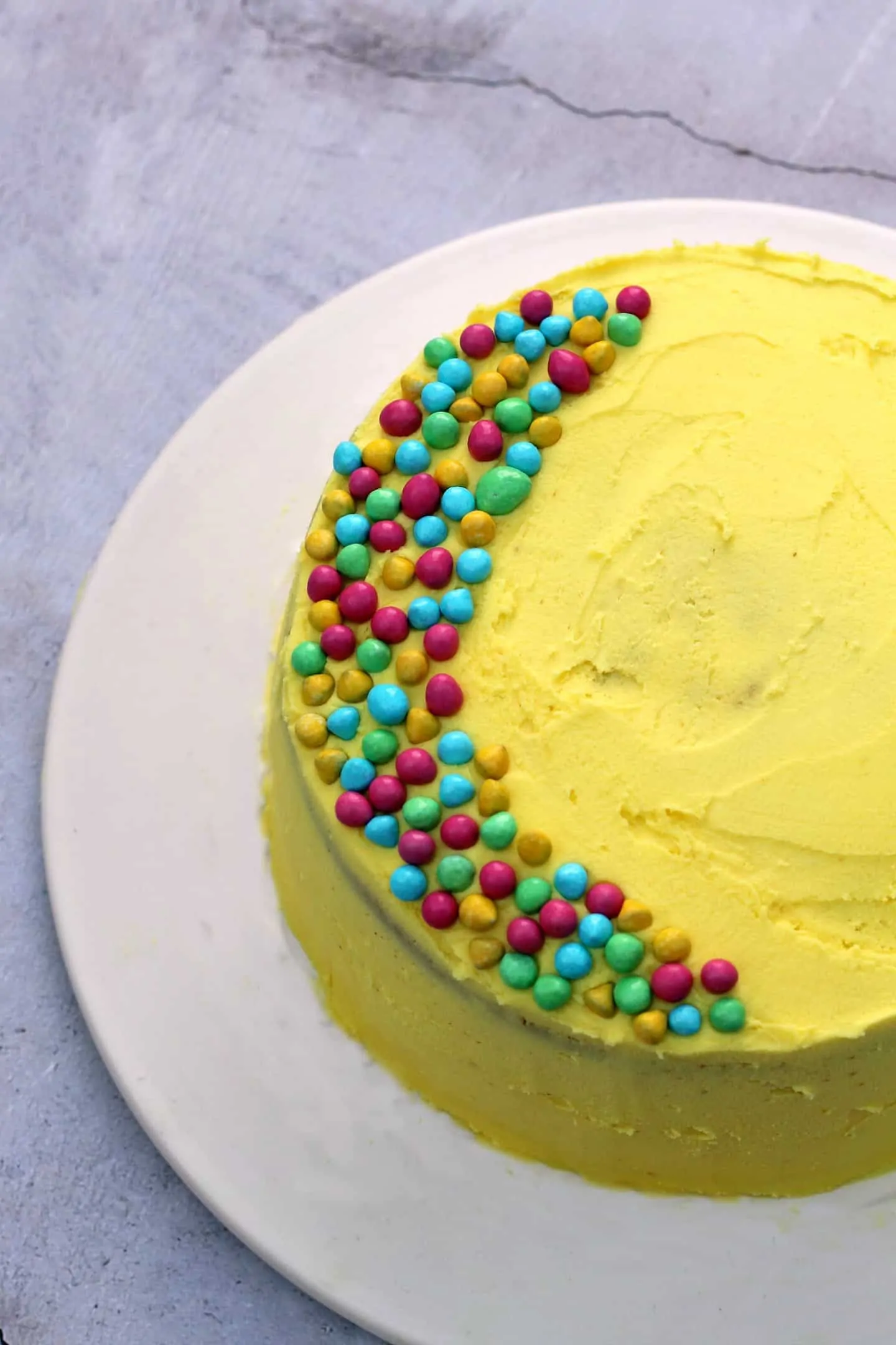 Close up of top of a yellow cake with multicoloured sprinkles.