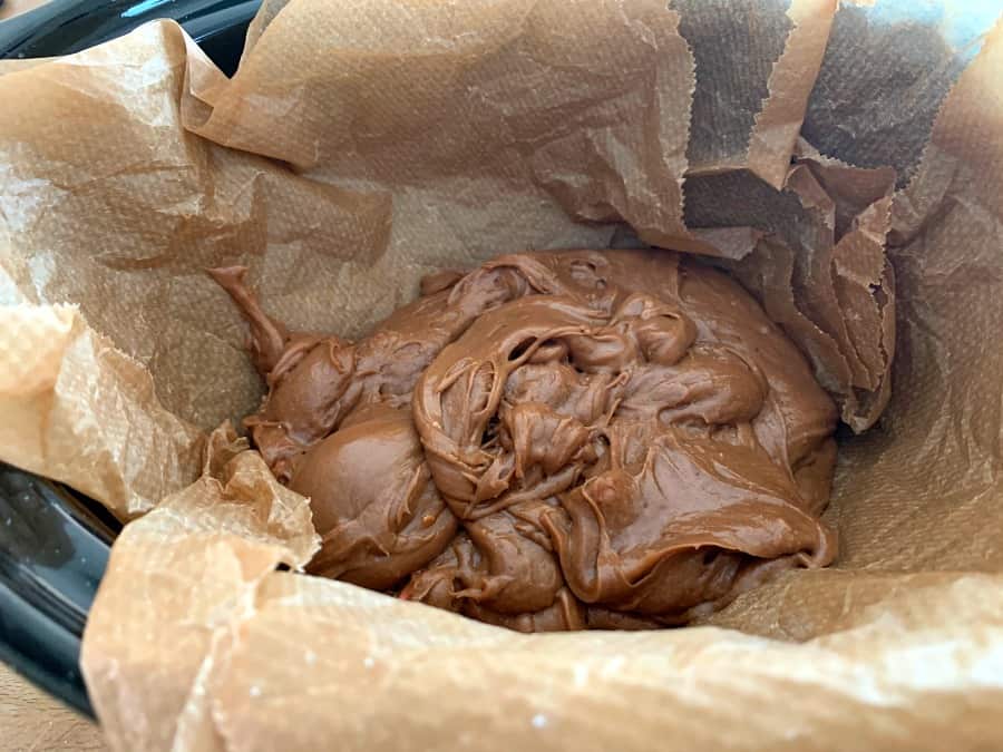 Brownie batter poured into slow cooker pot lined with baking paper.