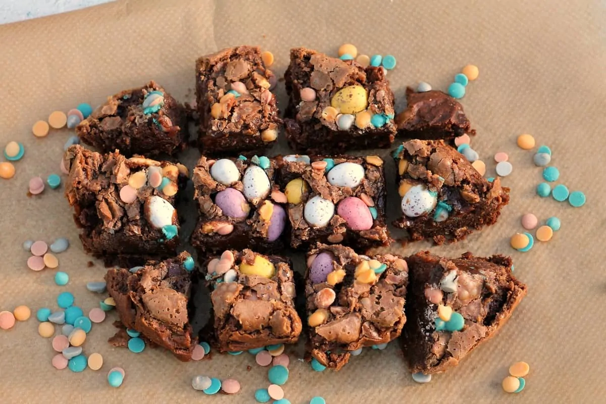 Squares of brownies with Mini eggs on top, on baking paper.