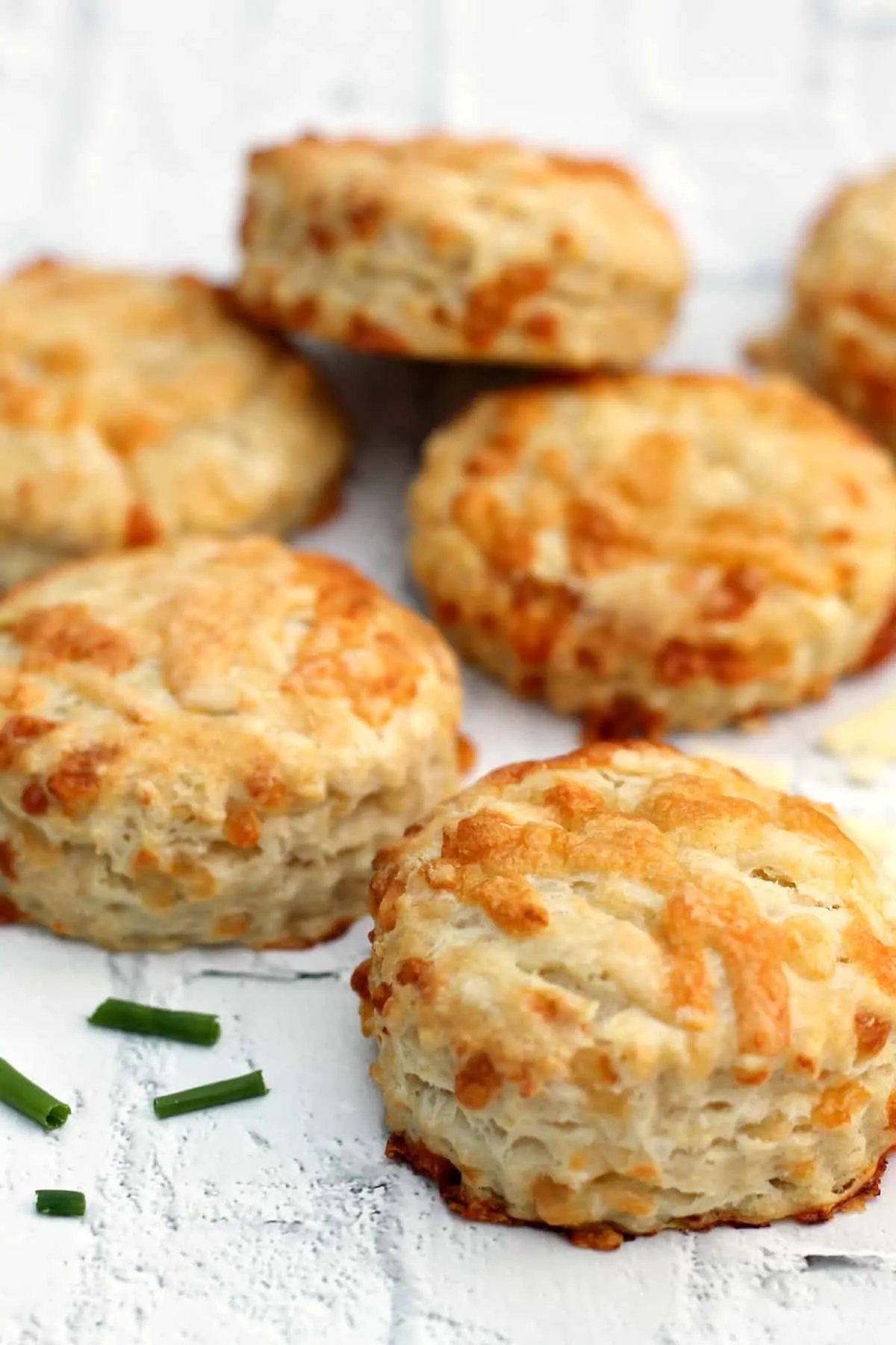 Close up of several cheese scones on white background, with snipped chives.