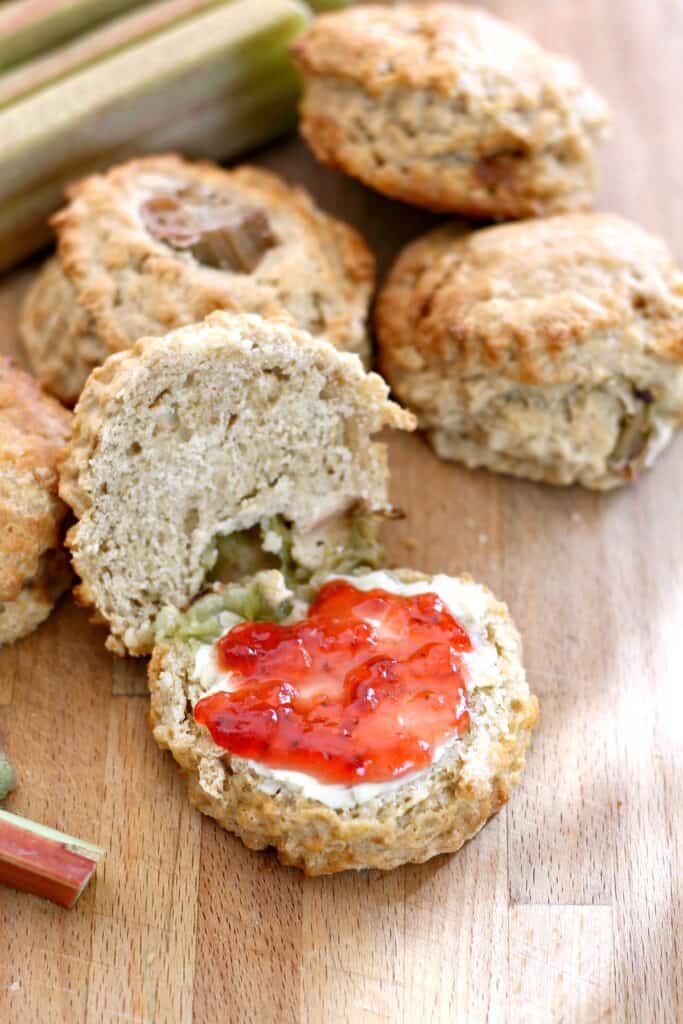 Scones on a wooden board, once sliced open and filled with jam.