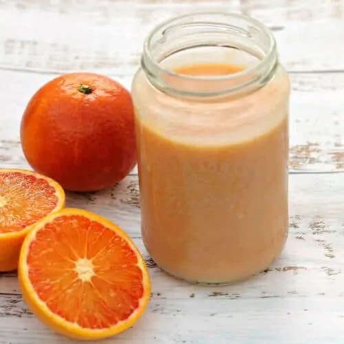 Jar of orange curd with oranges on a white wooden background.