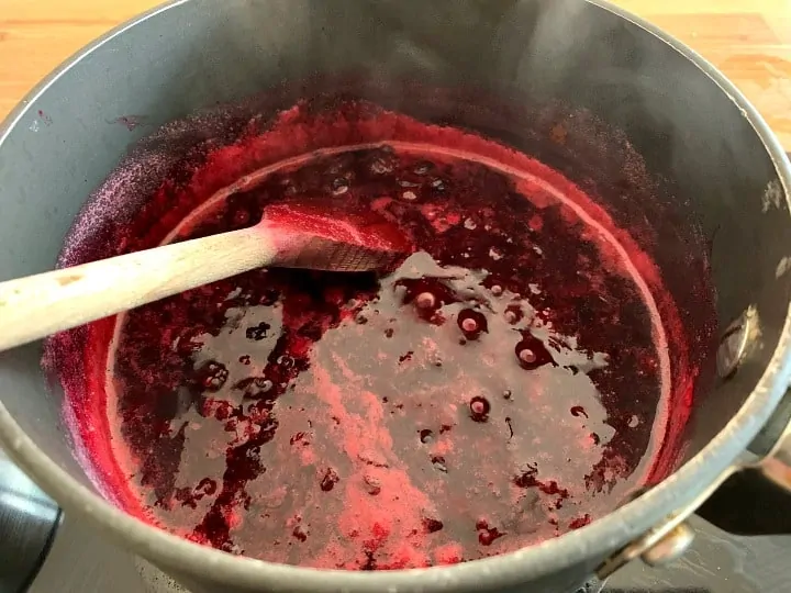 Saucepan with soft blackcurrants in water, after cooking to soften.