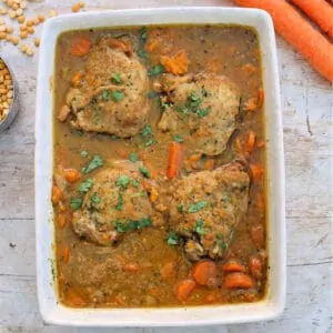 Chicken casserole in white serving dish, carrots and lentils in background.