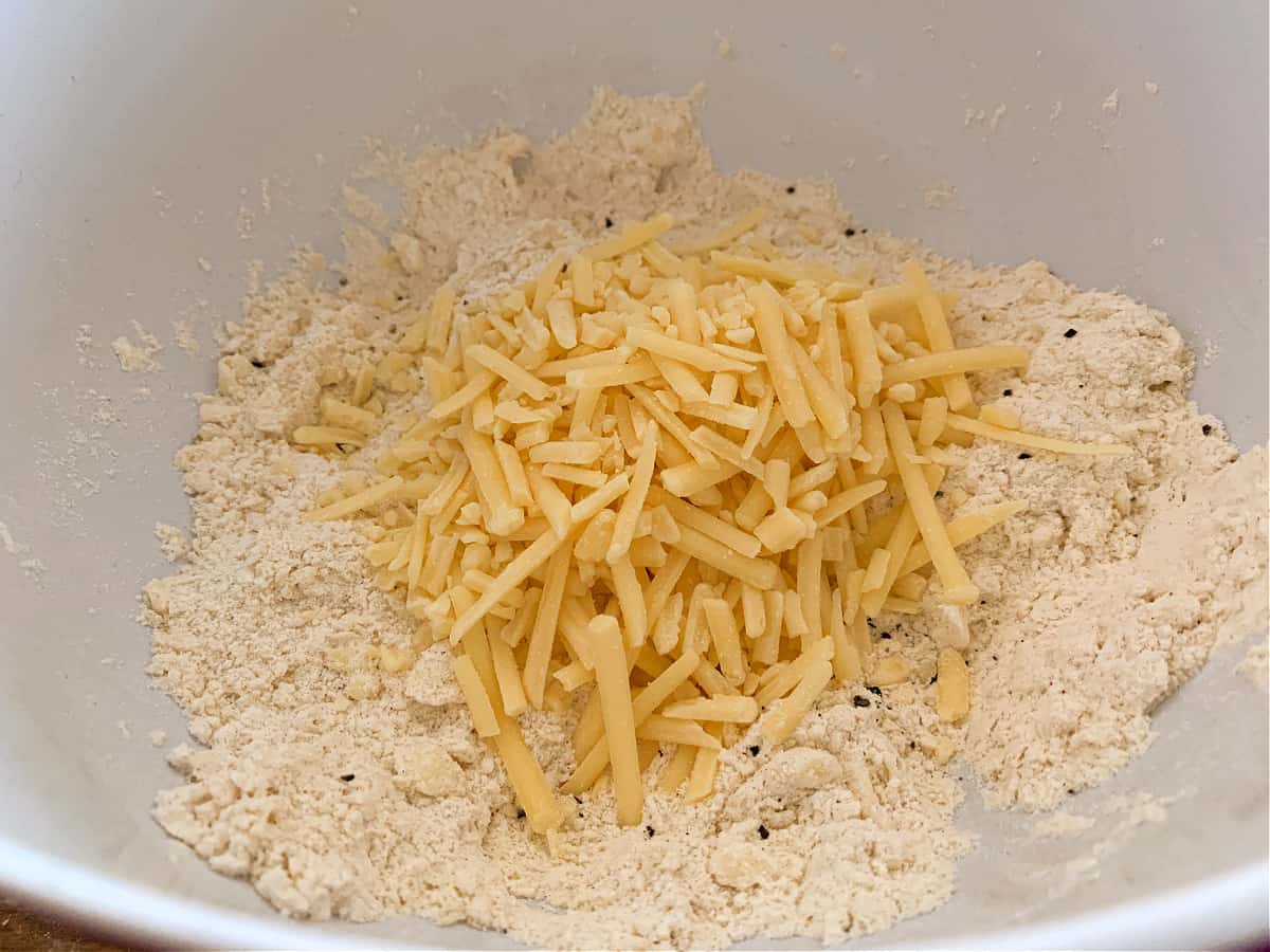 Cheese scones ingredients in a white bowl, grated cheese and seasoning added.
