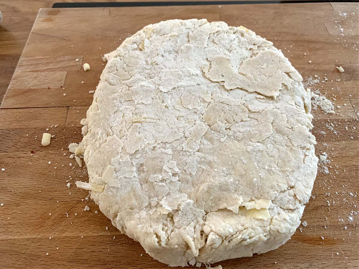 Scone dough on a wooden board, rolled out into a flat round shape.