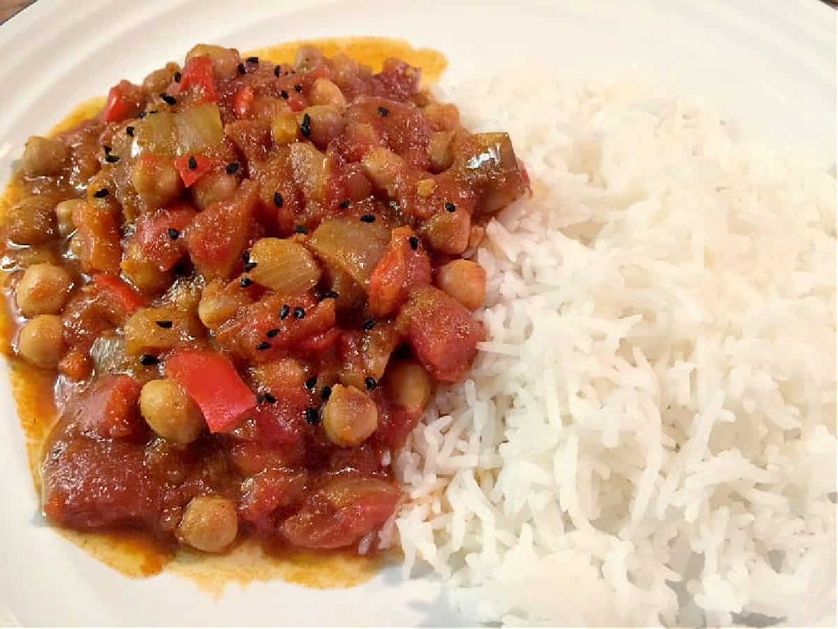 Curry served on a white plate topped with onion seeds, with white rice.