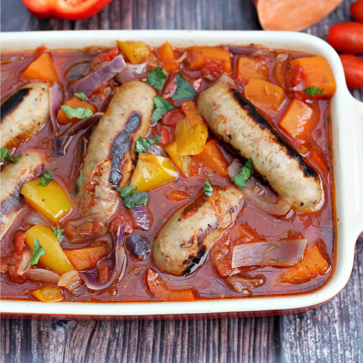 Sausage and vegetable casserole in a serving dish on a wooden background.