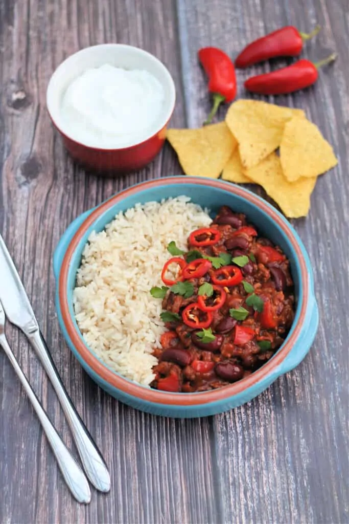 Bowl of chilli and rice with tortilla chips, sour cream and chillis.