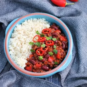Overhead view of bowl of chilli and rice on grey fabric.