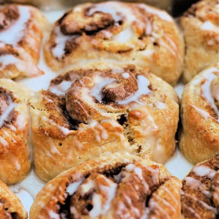Close up of cinnamon swirls with icing drizzled over in baking tin.