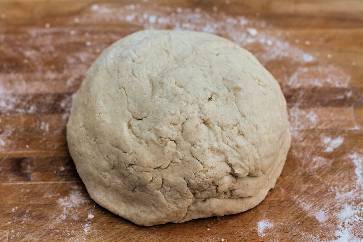 Scone dough in a ball on wooden chopping board.