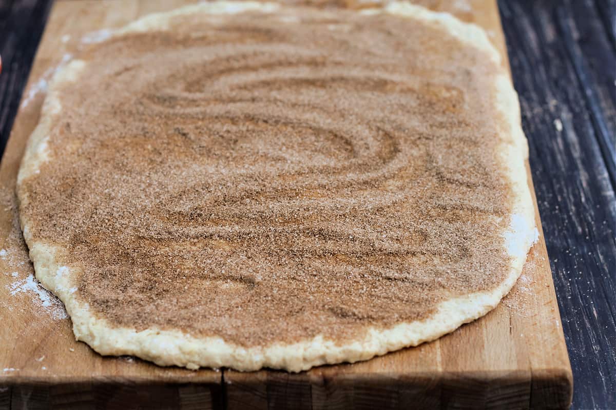 Rectangle of dough with cinnamon sugar topping on a wooden board.