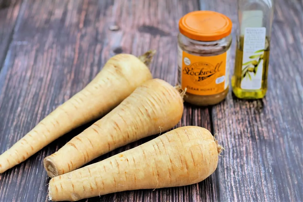 Some parsnips, a jar of honey and a bottle of oil on a wooden surface.