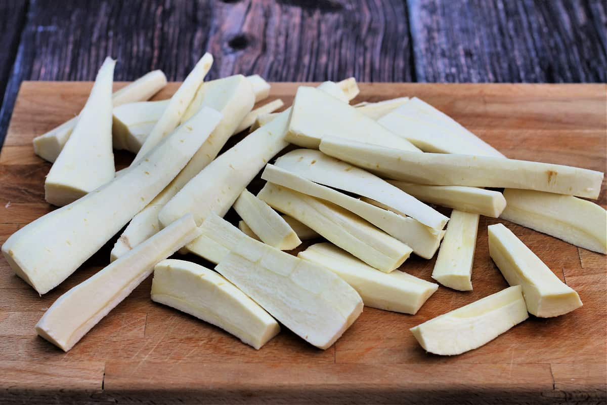 Sliced parsnips on wooden chopping board.