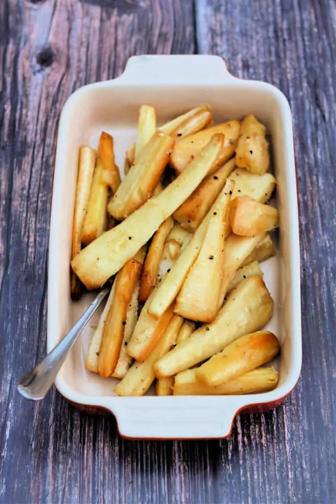 Roast parsnips made in the slow cooker in a serving dish with spoon.