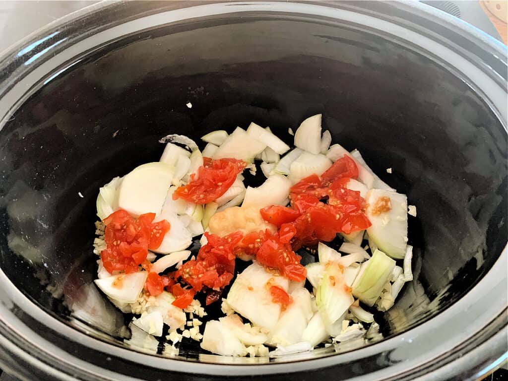 Onion, garlic, ginger and chopped tomatoes in slow cooker pot.