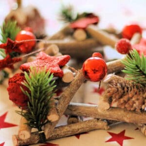 Christmas table decoration with pine needles and red baubles, on a table.