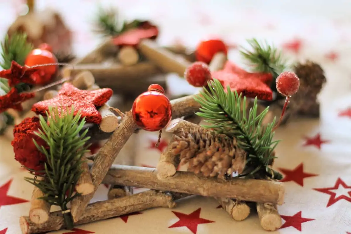 A festive wooden decoration with pine cones, red baubles and stars, on a table.