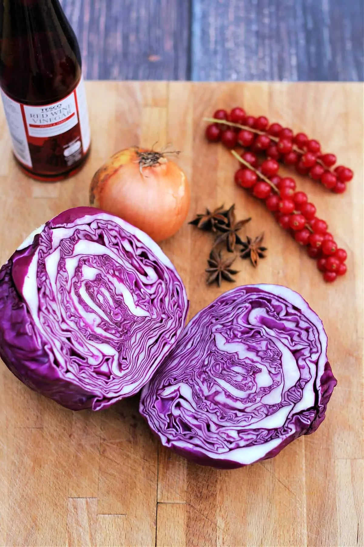 A halved red cabbage, onion, star anise and bottle of red wine vinegar on a board.