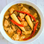 White dish with Chinese chicken curry with baby corn and red pepper.