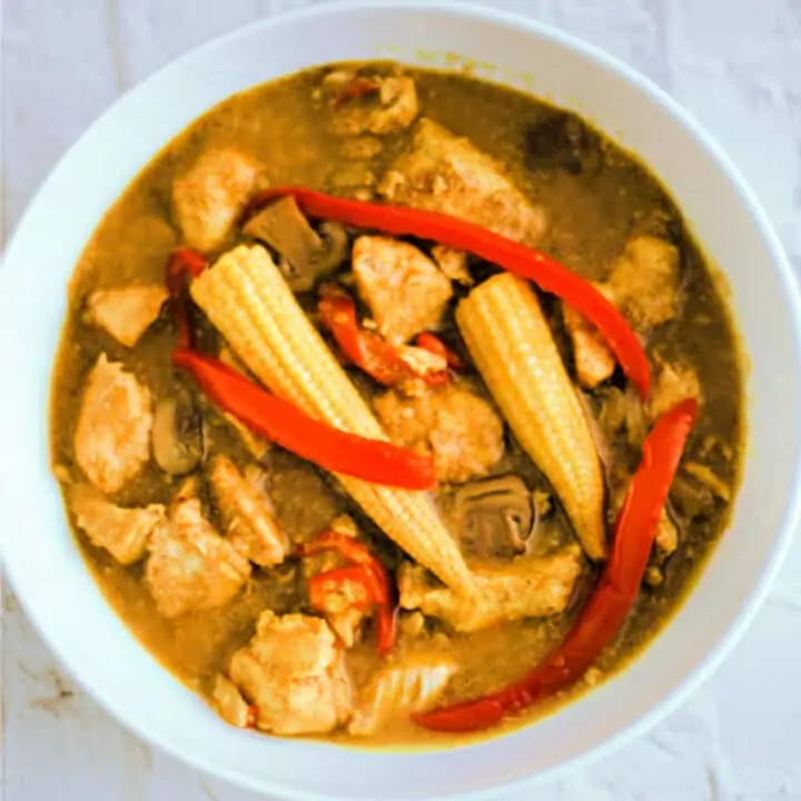 White dish with Chinese chicken curry with baby corn and red pepper.