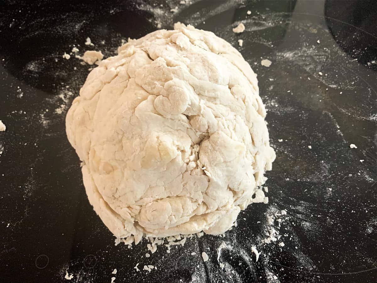 Rough ball of dough before kneading, on a black work surface.