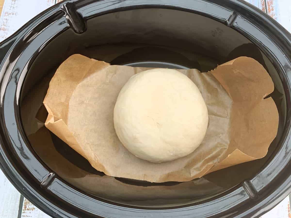 Ball of dough on a sheet of baking paper in slow cooker pot.