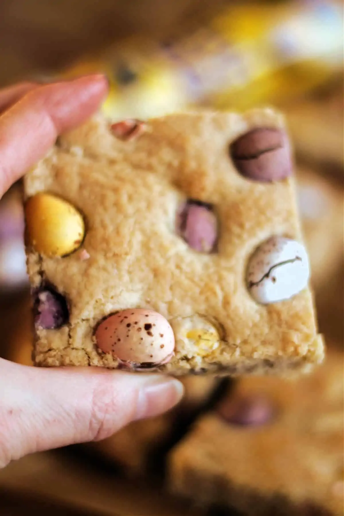 Hand holding a square cookie bar studded with chocolate mini eggs