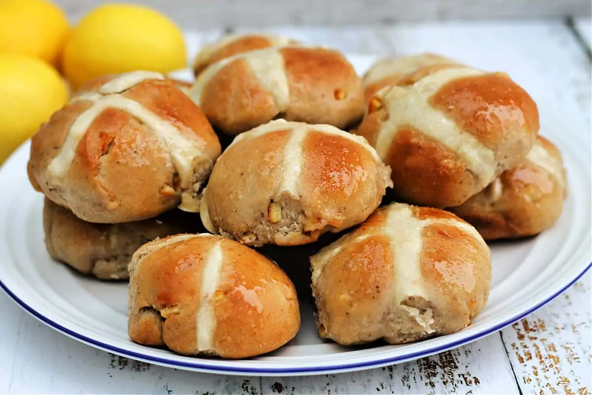 A pile of hot cross buns on a white plate.