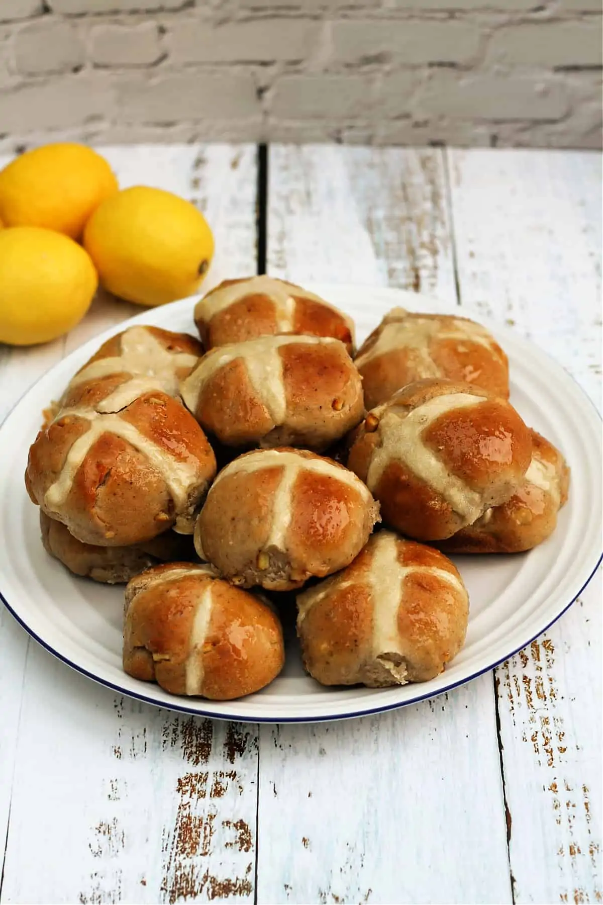 A white plate of hot cross buns, with lemons in the background.