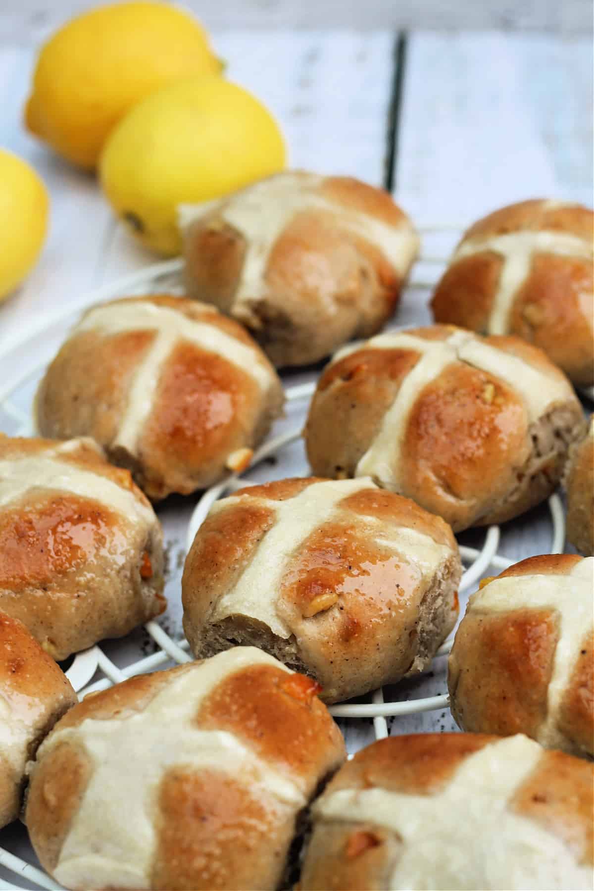 Hot cross buns on a cooling rack with lemons in background.