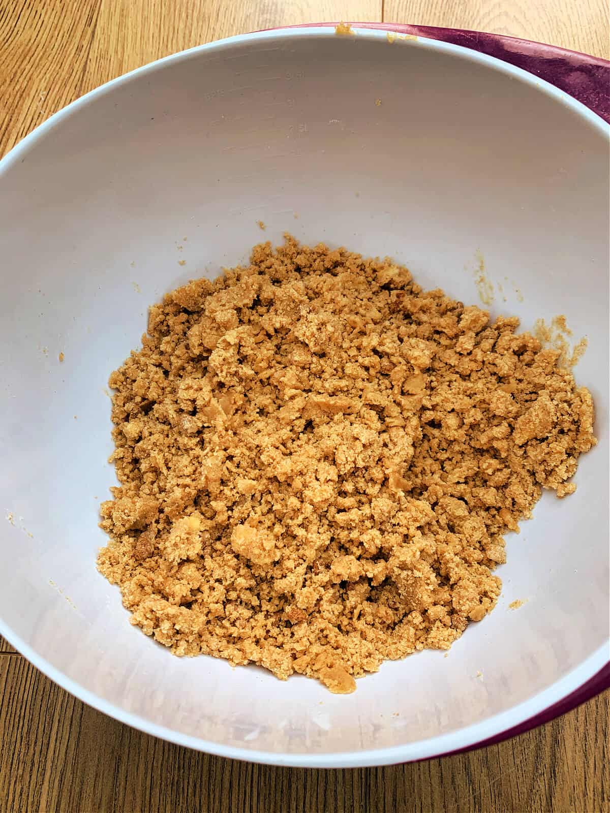 Flour, butter and brown sugar mixture in texture of fine breadcrumbs, in white bowl.