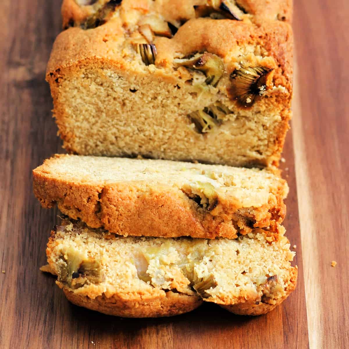 Sliced loaf cake with rhubarb inside, on a wooden board.