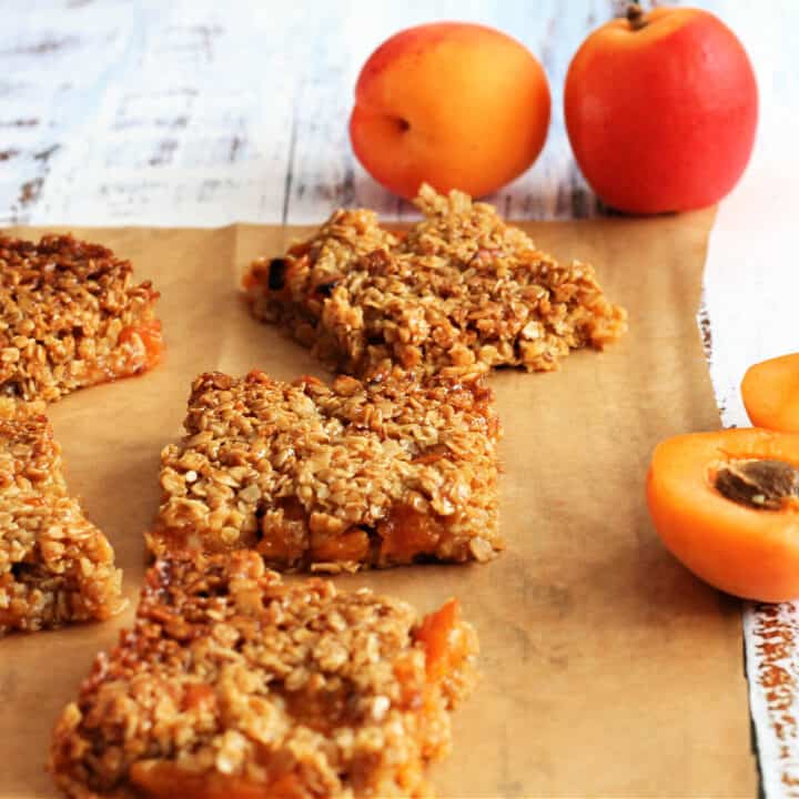 Squares of flapjack on baking parchment with fresh apricots scattered around.