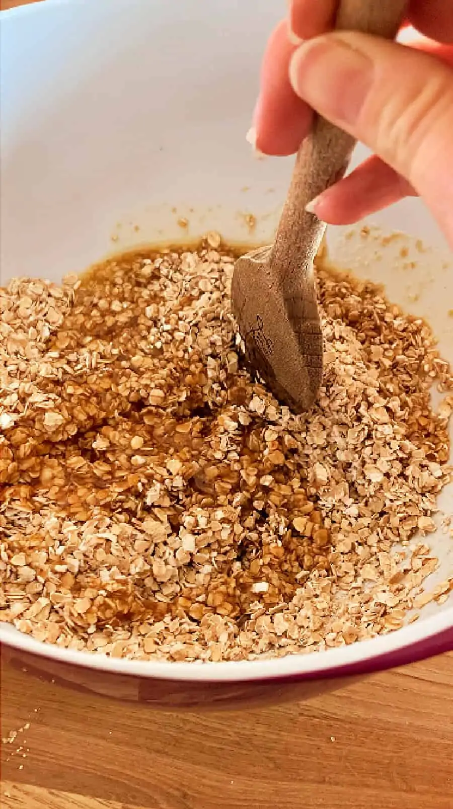 Image showing stirring the butter sugar mixture into oats using a wooden spoon.