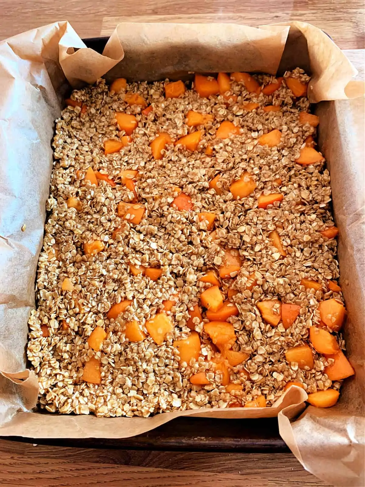 Lined baking tin with apricot flapjack mixture pressed evenly in.