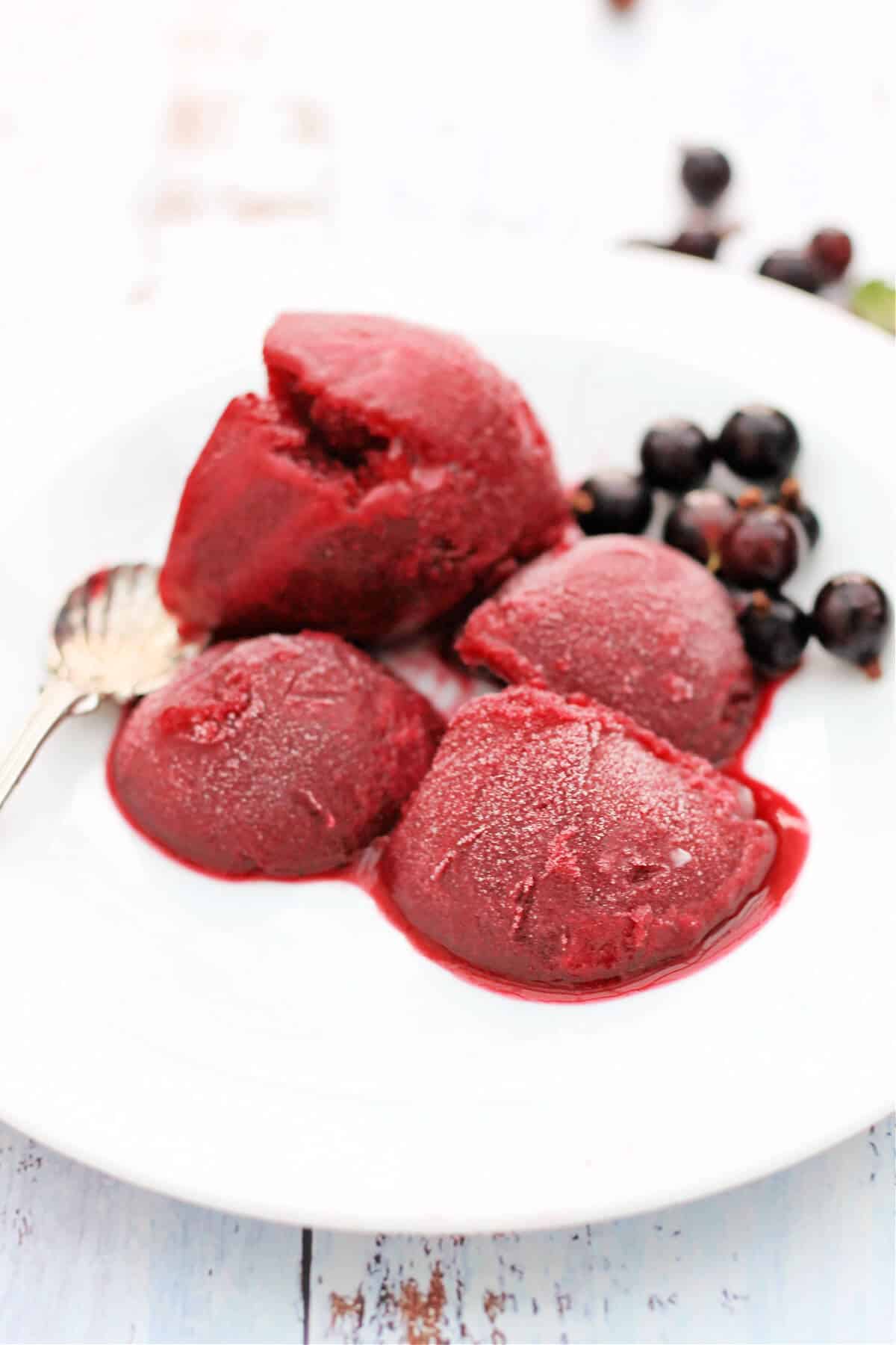 Four scoops of dark red sorbet on a white plate.