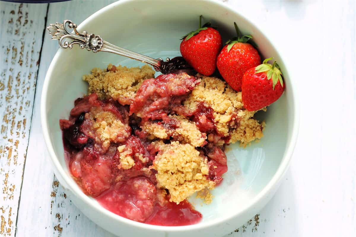 Close up of white bowl with serving of summer fruit crumble and berries.